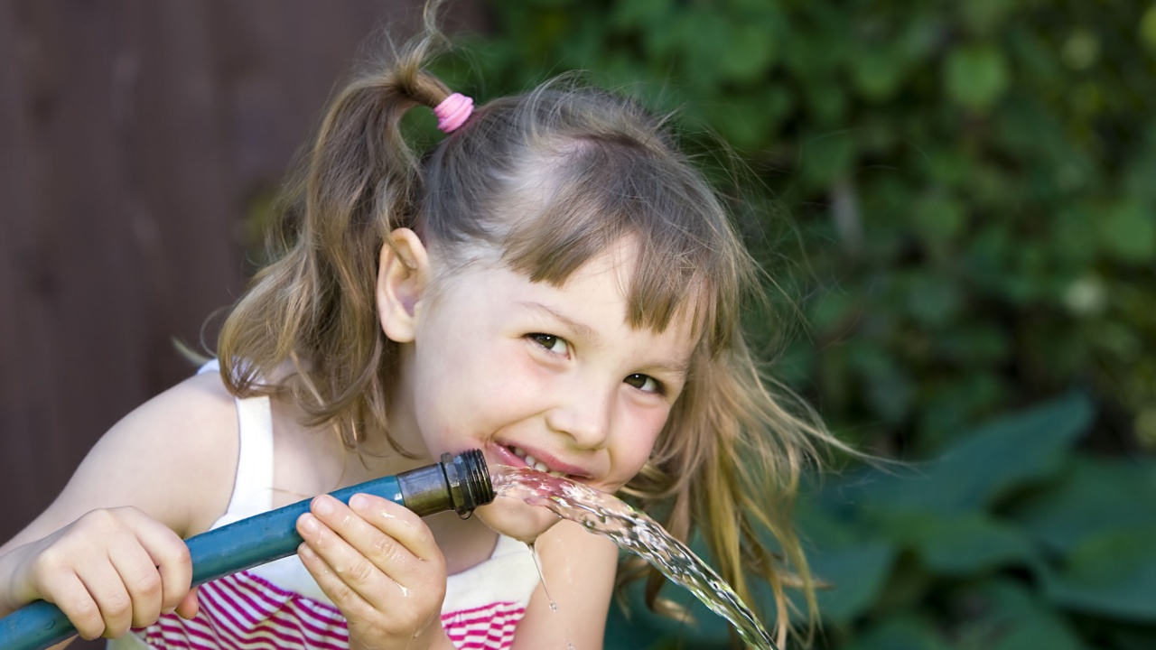 a cute child drinking from a garden hose
