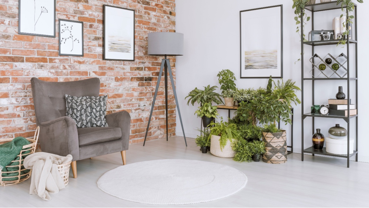 Baskets next to grey armchair with dark pillow against red brick wall in relax room with plants