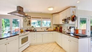 Large open white kitchen with beige floor and lots of windows.