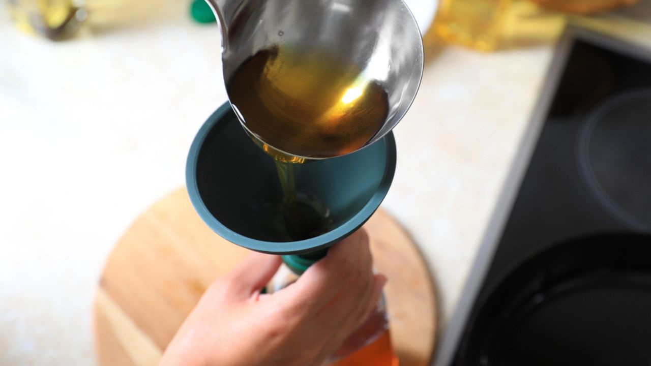 Woman pouring used cooking oil into bottle through funnel in kitchen, closeup