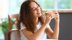 Young African-American woman with tasty sandwich in kitchen