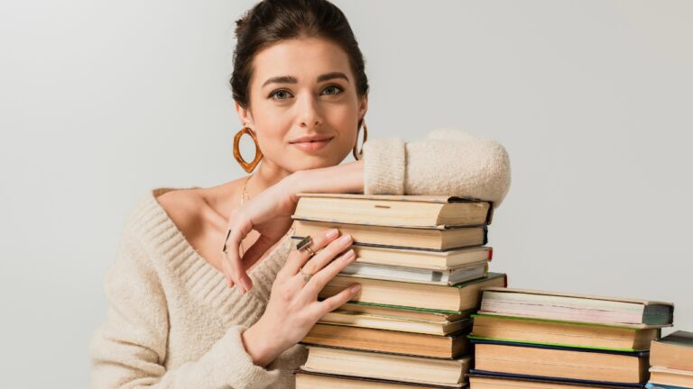a young woman smiles with a stack of books