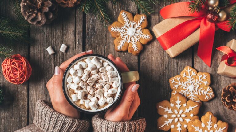 hands hold a mug of hot cocoa by christmas cookies