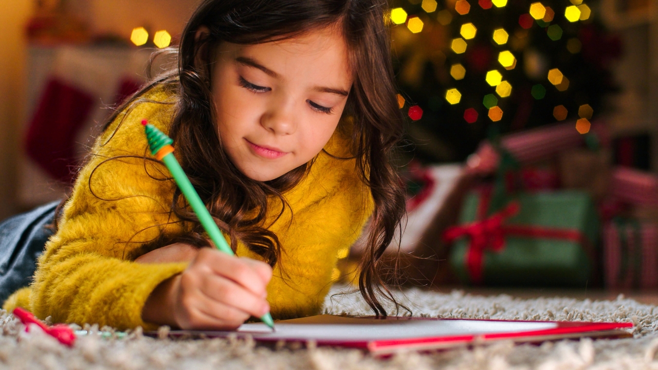 a little girl writing a note in front of a Christmas tree