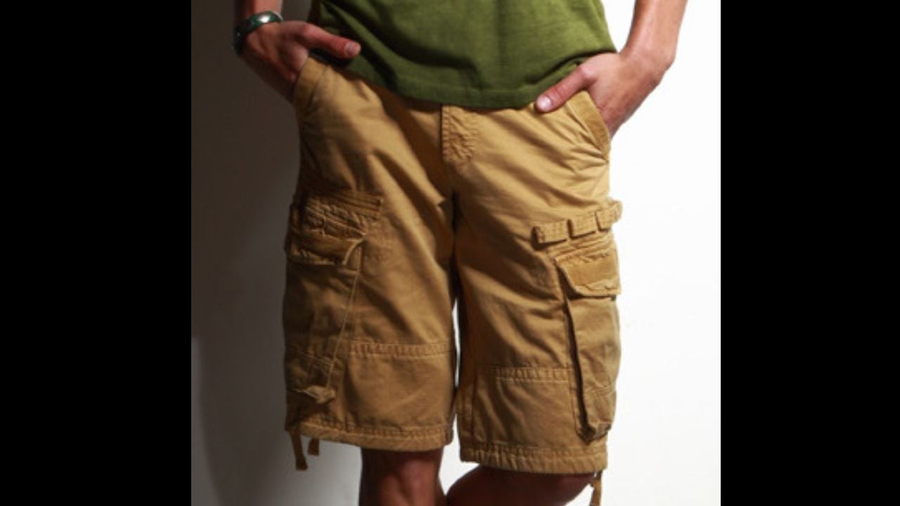 A standing man, wearing a green T-shirt, brown cargo shorts, and espadrilles.