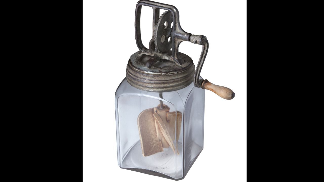 Antique glass butter churn with crank handle and wooden paddles isolated on white