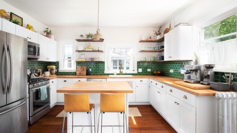 Elmhurst, IL, USA A renovated kitchen with white cabinets, a natural wood countertop, chairs sitting at the island, a green subway tile backsplash, and a gold pendant light.