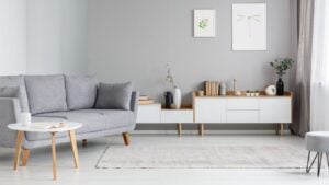 Grey settee near white cupboard in minimal living room interior with posters on the wall.