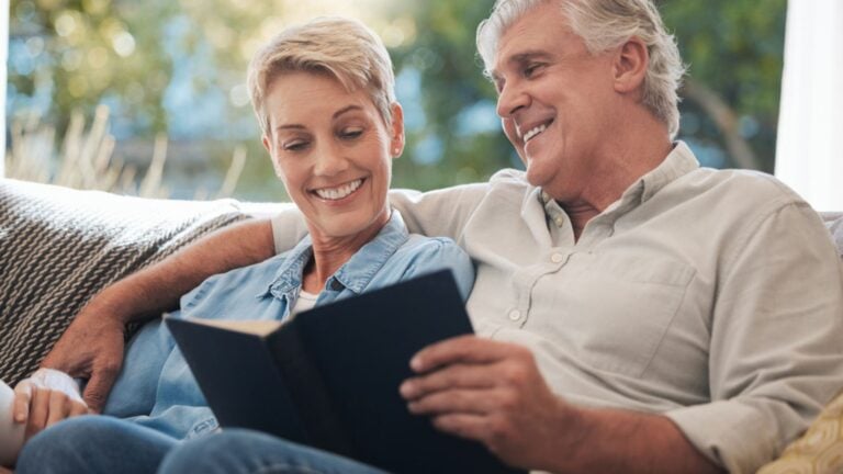 Love, calm and happiness mindset of a elderly couple with books together looking at pages of a book on a house couch