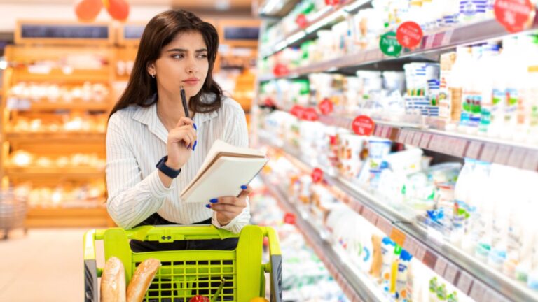 Middle Eastern Woman Doing Grocery Shopping Calculating Prices In Supermarket