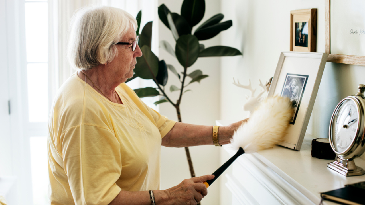 old woman dusting her mantel houseplant in background photo frame