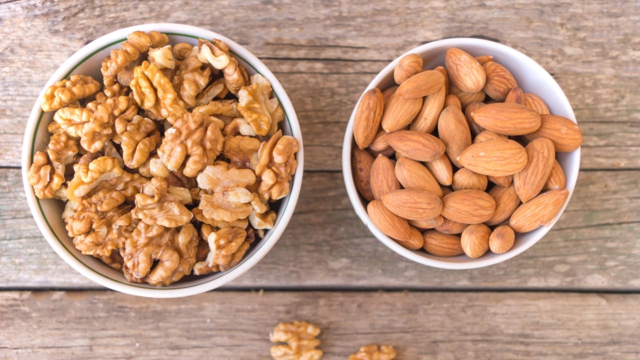 Two ceramic bowls full of walnuts and almonds on the wooden table