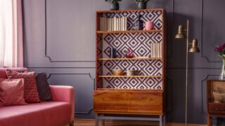 Renovated wooden bookcase with geometrical pattern and a brass floor lamp in a classy, dark living room interior with a comfortable pink settee
