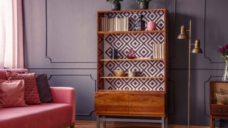Renovated wooden bookcase with geometrical pattern and a brass floor lamp in a classy, dark living room interior with a comfortable pink settee