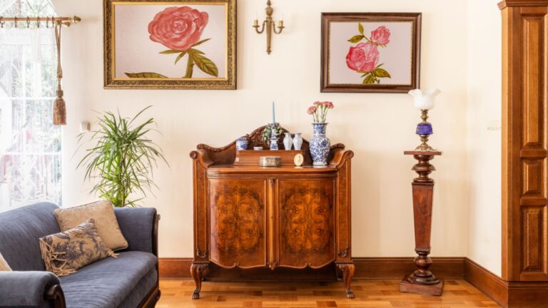 Real photo of an antique cabinet with porcelain decorations, paintings with roses and blue sofa in a living room interior