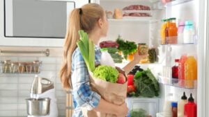 Woman putting products into refrigerator in kitchen