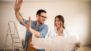 Young couple standing in their apartment while woman holding blueprint and man showing to her new ideas.