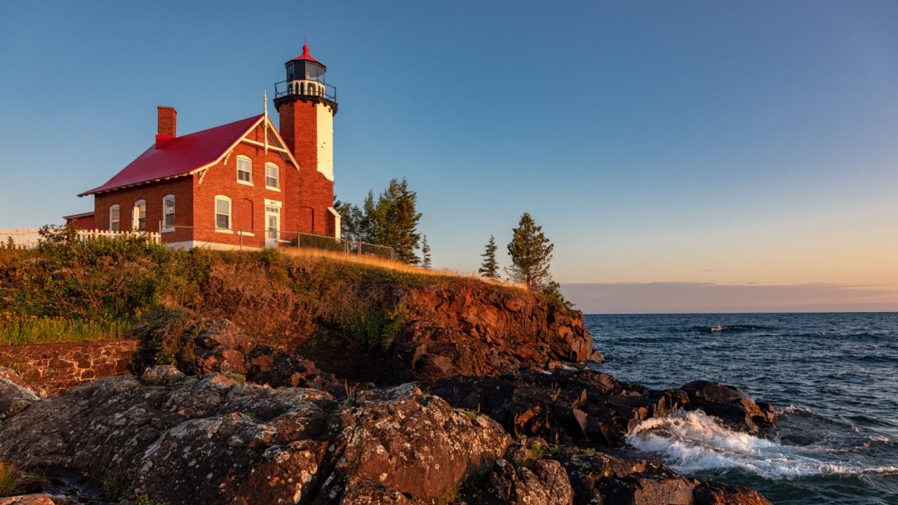 Early morning sunrise illuminates the rocks and front of Eagle Harbor Light on the Keweenaw Peninsula in Michigans Upper Peninsula. Waves from Lake Superior wash against the rocks.