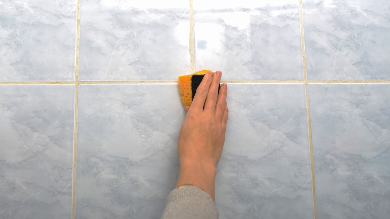 A woman wipes a tile in protective gloves in the bathroom with a detergent