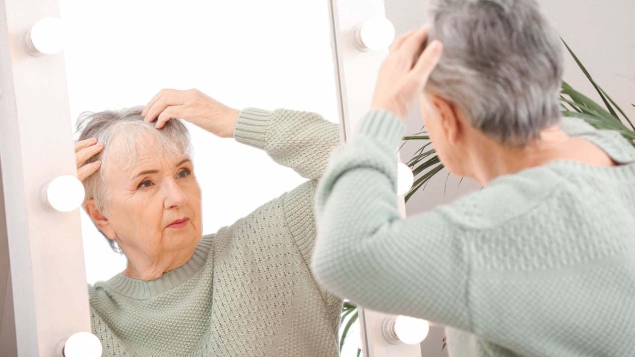 Senior woman with hair loss problem near mirror