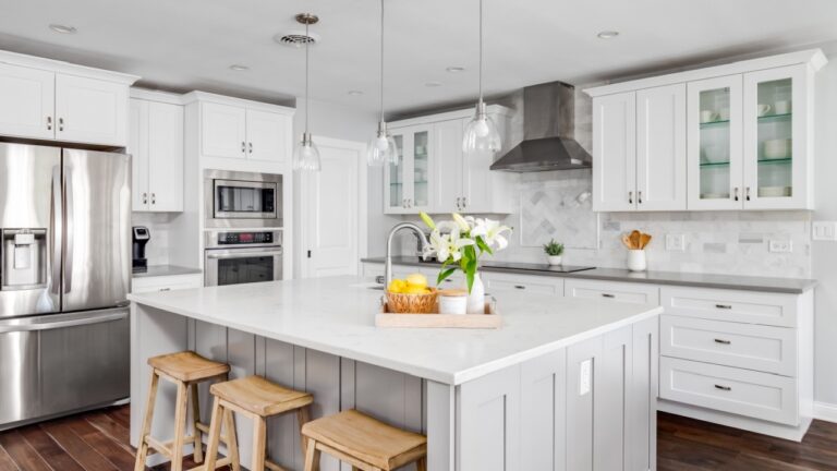ELMHURST, IL, USA - AUGUST 4, 2020: A large luxurious white kitchen with hardwood floors, bar stools, custom tiles, and stainless steel appliances. Lights off.