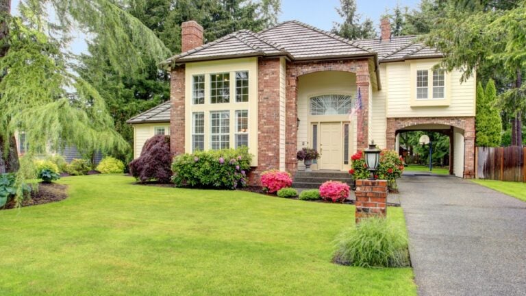 Beautiful curb appeal. Large brick house with siding trim and tile roof. View of entrance high ceiling porch and driveway with arch