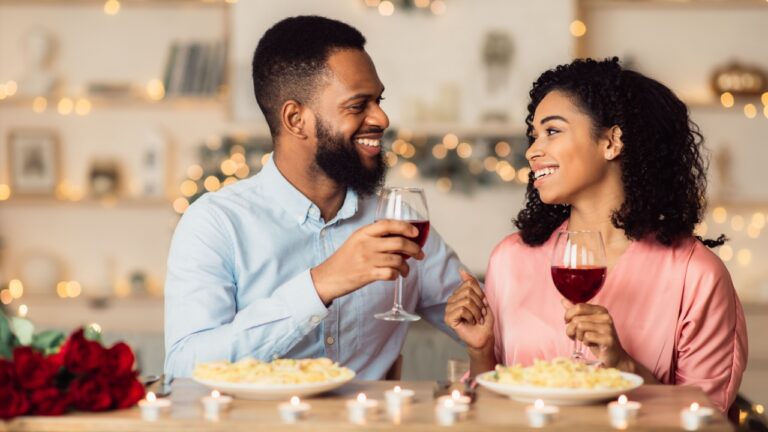 Handsome black man and pretty woman drinking wine at restaurant, toasting and celebrating Valentine's Day together. Couple of sweethearts having romantic dinner, enjoying festive meal in the evening