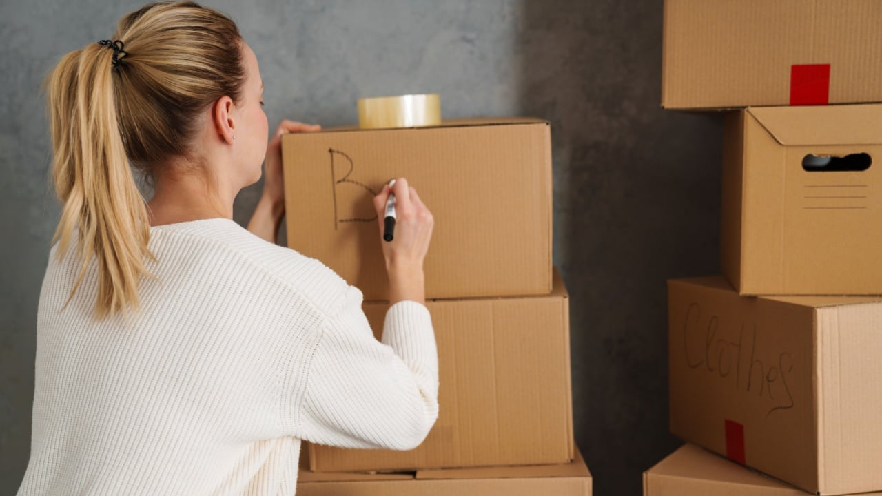 Smiling attractive young woman moving out from her old house, naming boxes