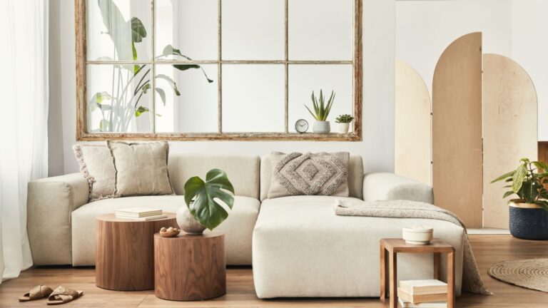 Modern interior of open space with design modular sofa, furniture, wooden coffee tables, plaid, pillows, tropical plants and elegant personal accessories in stylish home decor. Neutral living room.