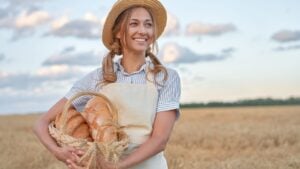 Female farmer standing wheat agricultural field Woman baker holding wicker basket bread eco product Baking small business Caucasian person dressed straw hat apron organic