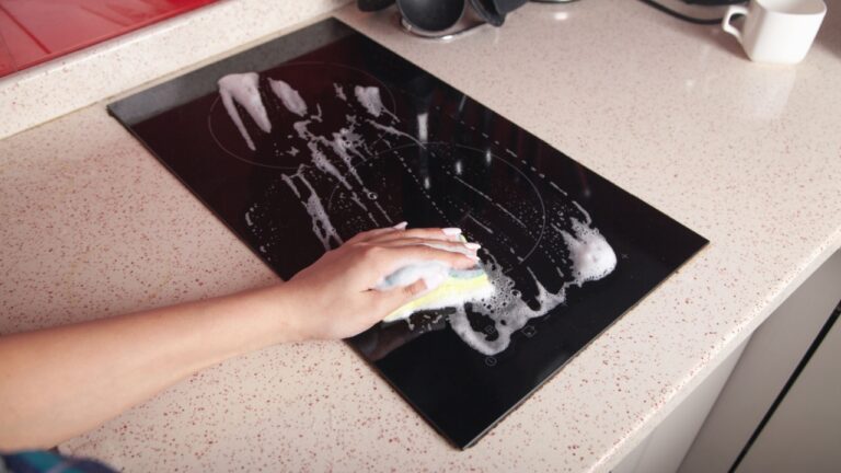 Woman washing modern electric stove in kitchen.