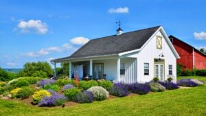 Traditional style farmhouse with porch, in upstate New York. A nice flower garden, and a red barn in back.