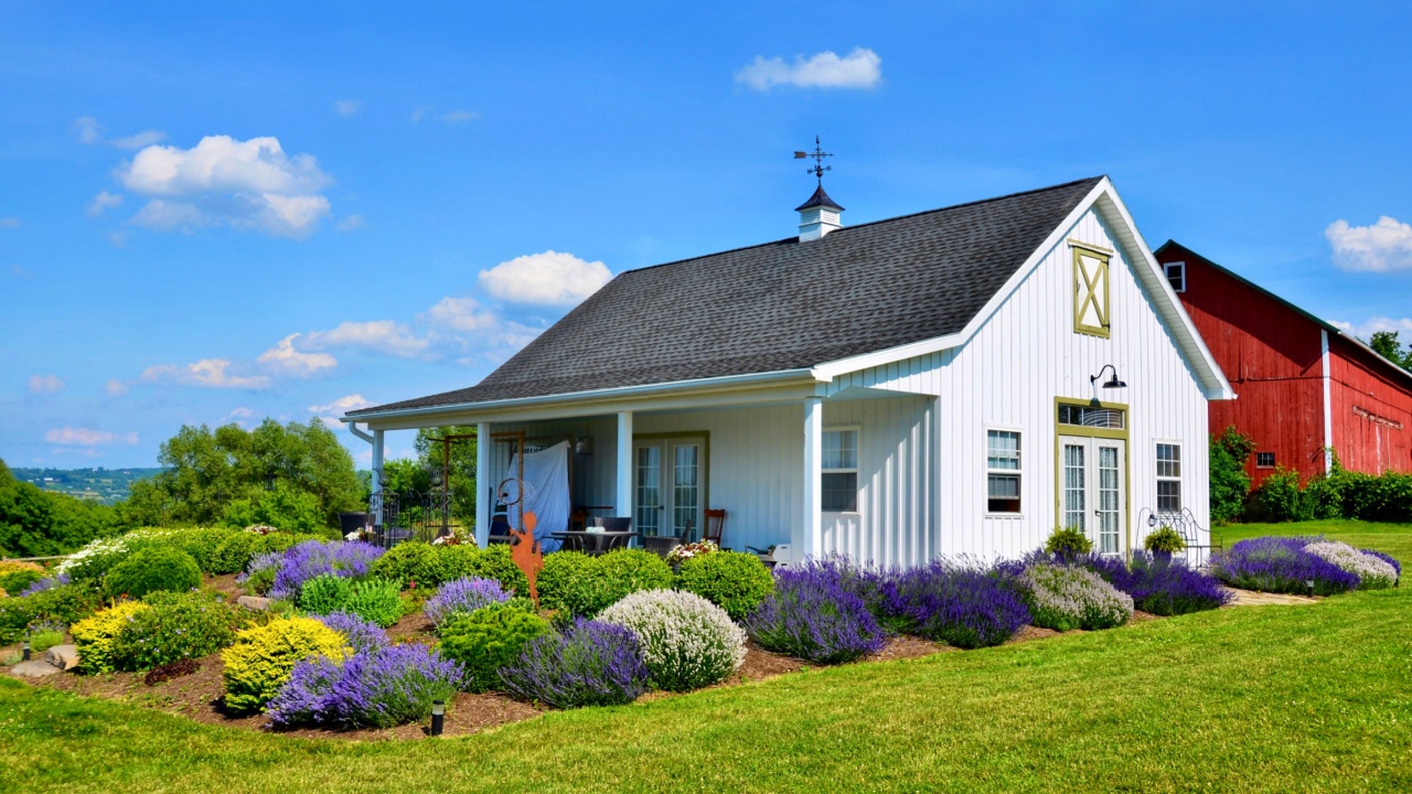 Traditional style farmhouse with porch, in upstate New York. A nice flower garden, and a red barn in back.