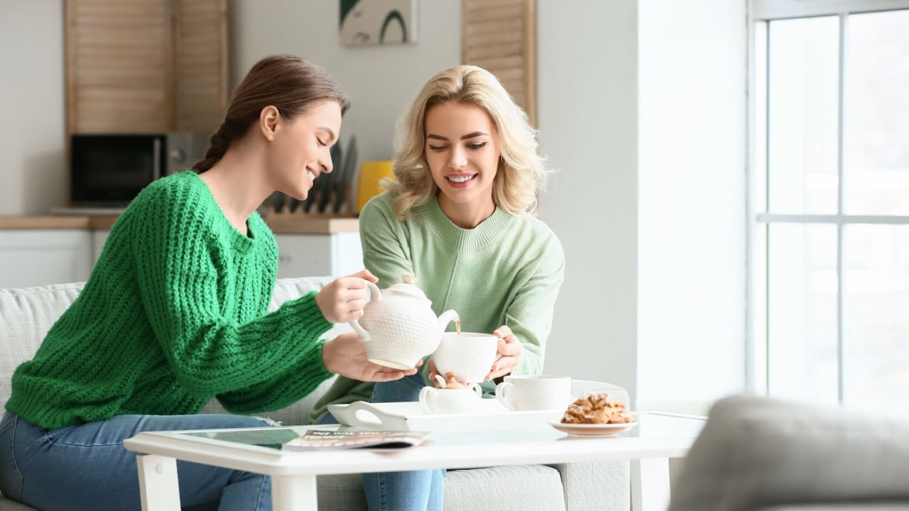 Beautiful young sisters drinking tea at home