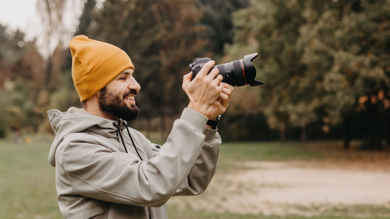 stylish bearded photographer with a camera in his hands takes a photo in the autumn park