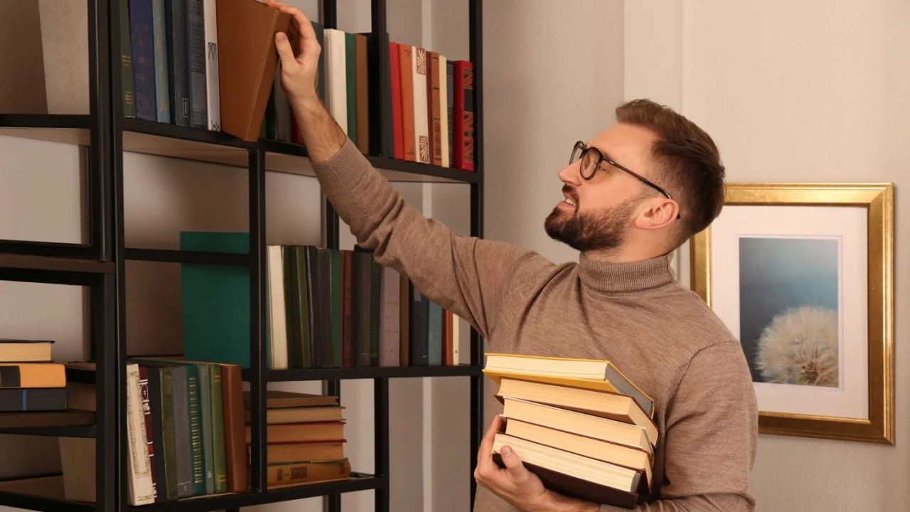 Young man choosing books on shelf in home library