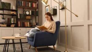 Young woman reading book in armchair indoors. Home library