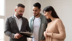 Buying New House. Smiling young Arab spouses discussing agreement with real estate agent or broker. Professional financial advisor or salesman explaining contract details to clients at meeting