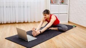 Healthy lifestyle concept. Yoga, fitness, meditation. Young sporty woman practicing yoga. Woman exercising at home in front of her laptop, stretching her leg.
