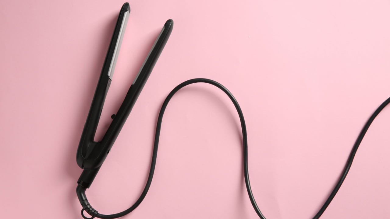 Modern flat hair iron on pink background, top view