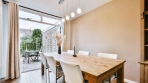 Living room with wooden cabinet near dining zone and table and chairs against big opened doors to backyard with beige walls and parquet