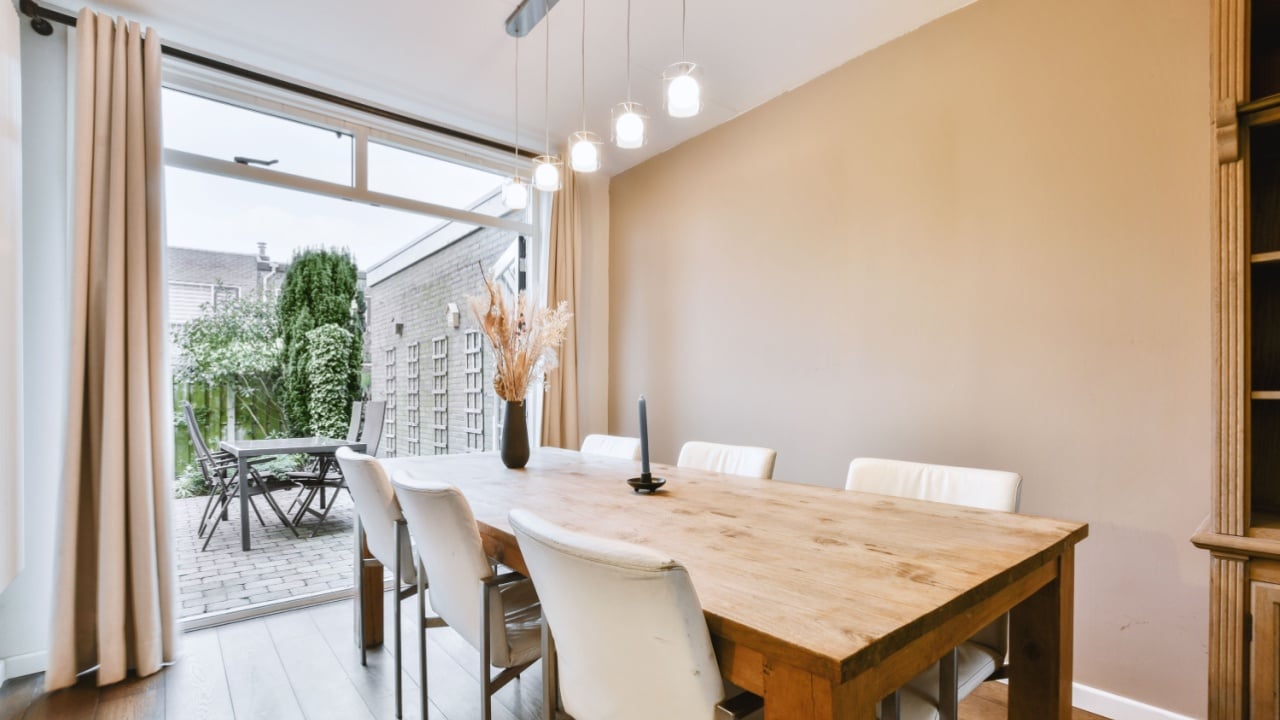 Living room with wooden cabinet near dining zone and table and chairs against big opened doors to backyard with beige walls and parquet