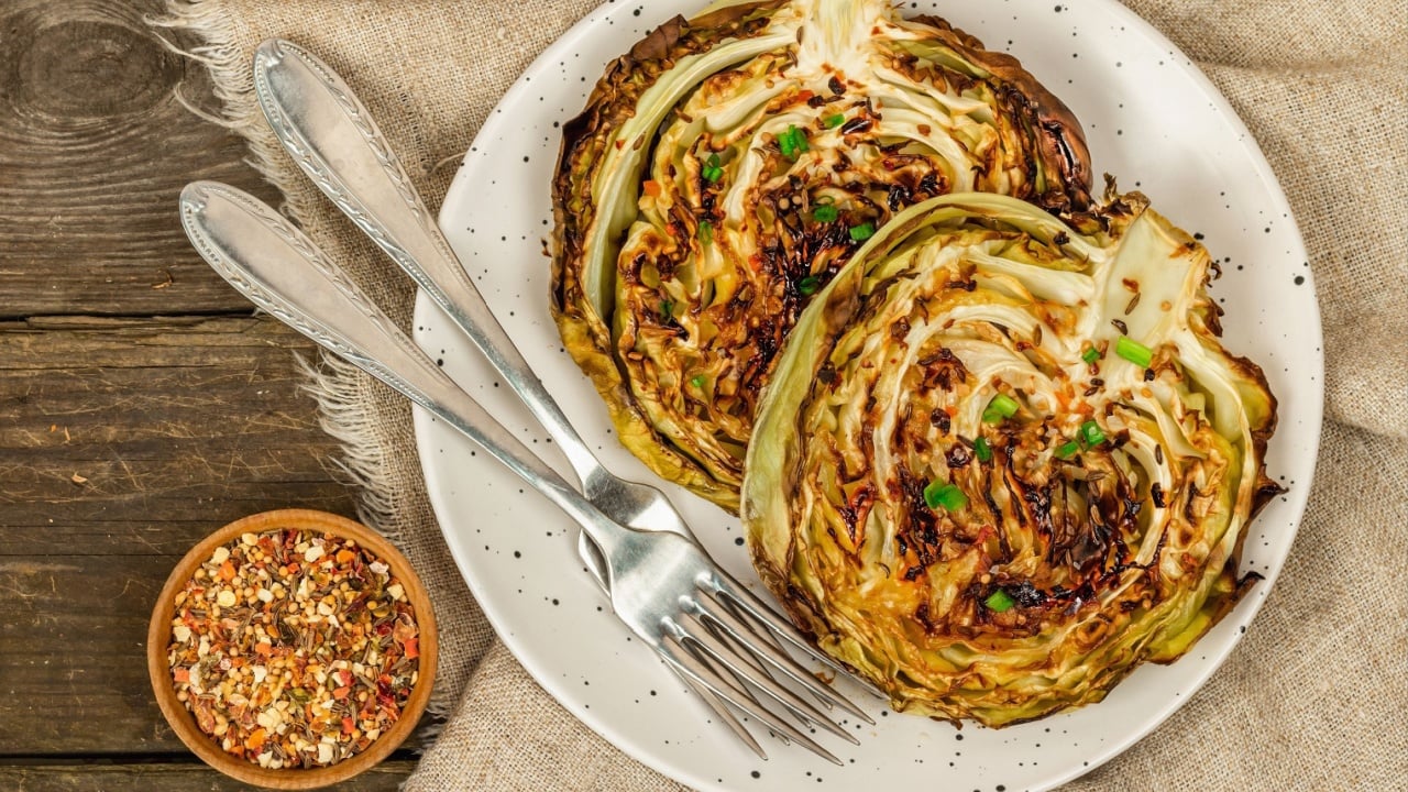 Homemade vegan cabbage steaks with herbs and spices. Healthy food ready to eat on a serving plate, cutlery. Old wooden background, top view