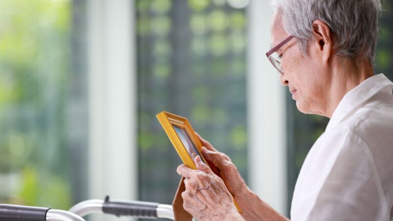 Sad old elderly with depression looks at photograph of her family with nostalgia,remembrance,Depressed asian senior woman patient holding picture frame, sitting alone in loneliness at nursing home
