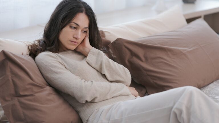 Sad young woman sitting on the bed at home, she is lonely and depressed