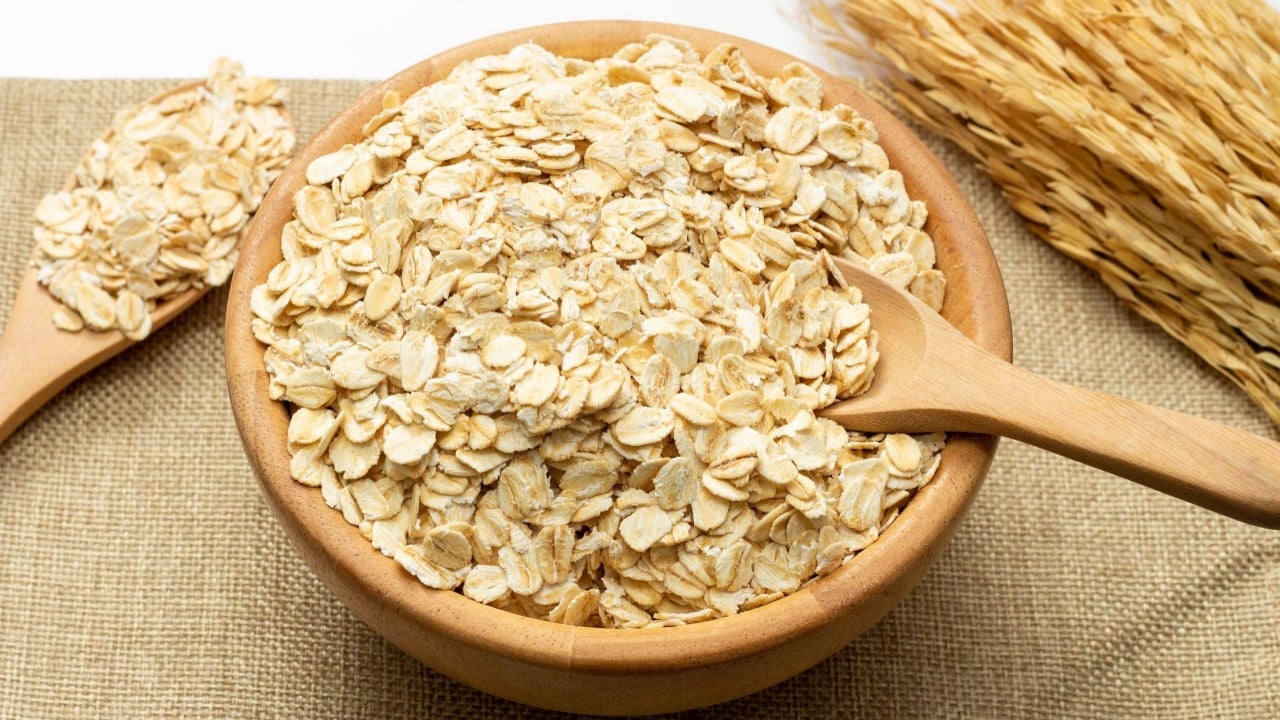 Concept of healthy grain, Oat flakes or oat cereal in spoon and wood bowl on linen cloth background.