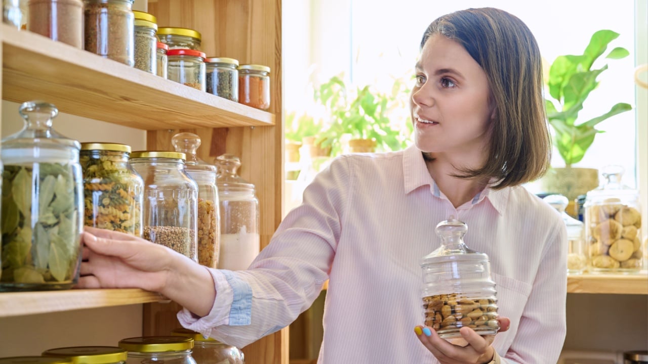 Young woman in kitchen with containers jars of food, holding jar of almonds