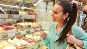 Young woman is looking for cakes on the cooling shelf in a cafe or pastry shop