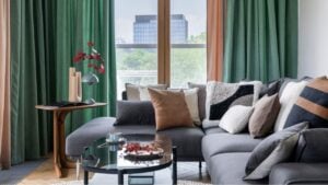 Cozy living room interior with modern gray sofa, pillows, glass coffee table, green curtain, big window, beige vase with dried flowers, stand lamp and personal accessories. Home decor. Template.