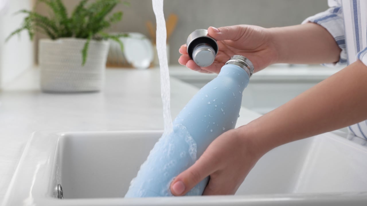 Woman washing thermo bottle in kitchen.